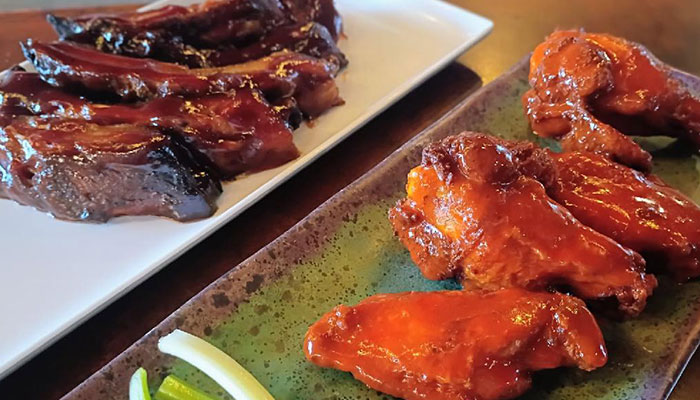 The 208 Bar & Grill Specials: Barbecue ribs and chicken wings with celery and dip on rectangular plates.